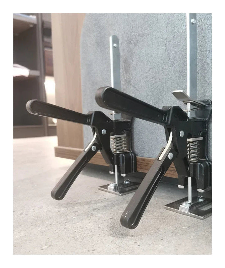 Two board lifters holding a cabinet panel clear of the floor against a wall