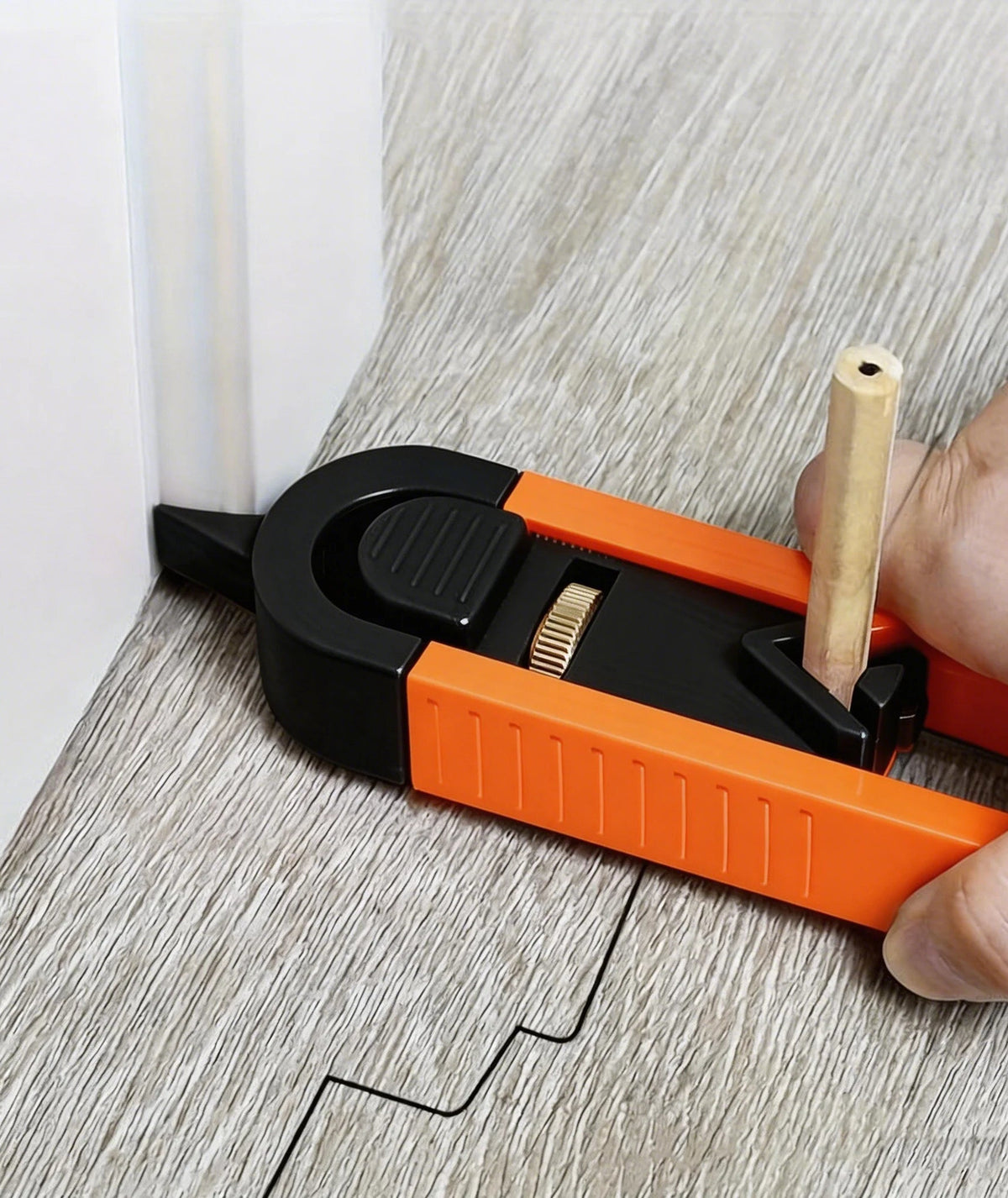 The scribing tool on a floor plank, its pointer against a white door casing and a pencil in the slide drawing the casing's outline on the plank