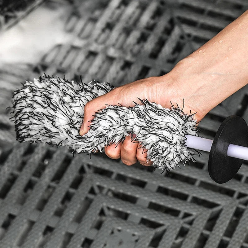 A hand squeezing the plush microfiber head of the black and white wheel brush